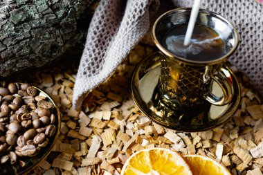 Aromatik koyu kahve, yüzeyinde baloncuklar olan sütlü çay tabağında, tam tahıllı, soyulmuş ve kurutulmuş portakalların yanında. Arkaplanda kızılağaç parçaları ve ahşap çıkıntıların arka planı