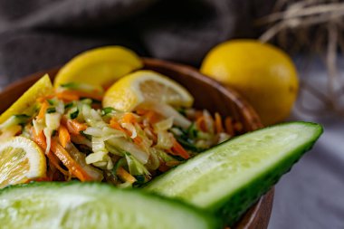 Derin bir tabakta taze sebzelerden oluşan sağlıklı bir salata. Beyaz lahana, havuç ve limon dilimleri ve otlarla süslenmiş mis kokulu salatalıkla dolu bir tabak. Sağlıklı beslenmenin ilginç bir sunumu