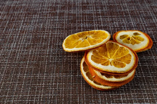 Composition of orange dried oranges slices of round shape, preserved color, on a mottled woven brown background. Citrus template for textural background design