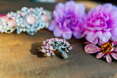 Eski ahşap bir yüzeyde pembe renkli kadın mücevherleri ve aksesuarları kompozisyonu. Renkli taşları, tokaları ve çiçekleri olan bir broş.