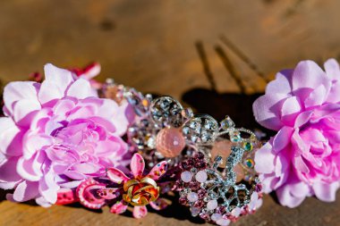 Eski ahşap bir yüzeyde pembe renkli kadın mücevherleri ve aksesuarları kompozisyonu. Renkli taşları, tokaları ve çiçekleri olan bir broş.