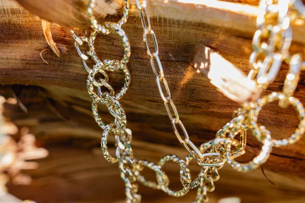 This season, multi-tiered chains of different types and sizes are fashionable. Faceted Golden links of the metal alloy dry hanging on the branches, bark and wood from the elements of nature. Details of decorations