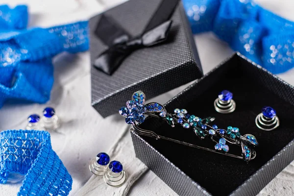 Beautiful brooch with blue and aquamarine stones and rhinestones of different sizes, metal base pins in a gift box with a black bow, around the ribbon with silver threads and springs.