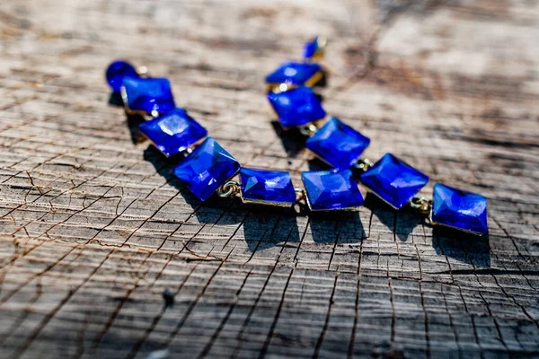 Costume jewelry for a festive day, long earrings with large square blue stones and an ultramarine bracelet. Elegant accessories on a dry wooden surface on natural elements