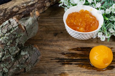 Kayısı ve şeftali reçeli tatlı olarak da portakal reçeli. Bütün bir meyvenin yanında, kayısılar şerbetle marine edilir. Eski ahşap arka plan ve kabuklu beyaz çiçekler