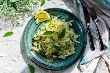 Taze sebzeli çıtır salata. Limonla süslenmiş salatalık ve roka yapraklı lahana ve çatal bıçaklı, hafif desenli taş bir masada bir buket beyaz çiçek.