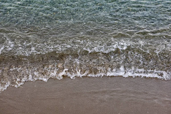 The surface is salty sea water, swaying in small waves near the shore, through the transparent bottom you can see stones and pebbles