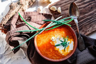 Kahverengi bir tabakta kırmızı borş, eski bir tahta tahtanın yanında sarımsak ve bıldırcın yumurtası, yeşil pırasa ve süzülen dallar. Çorbada beyaz ekşi krema, eski bir Polonya kaşığının yanında.