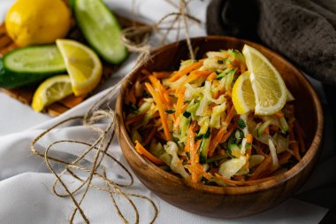 Derin bir tabakta taze sebzelerden oluşan sağlıklı bir salata. Beyaz lahana, havuç ve limon dilimleri ve otlarla süslenmiş mis kokulu salatalıkla dolu bir tabak. Sağlıklı beslenmenin ilginç bir sunumu