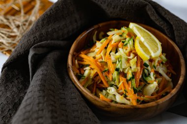 Derin bir tabakta taze sebzelerden oluşan sağlıklı bir salata. Beyaz lahana, havuç ve limon dilimleri ve otlarla süslenmiş mis kokulu salatalıkla dolu bir tabak. Sağlıklı beslenmenin ilginç bir sunumu