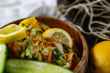 Derin bir tabakta taze sebzelerden oluşan sağlıklı bir salata. Beyaz lahana, havuç ve limon dilimleri ve otlarla süslenmiş mis kokulu salatalıkla dolu bir tabak. Sağlıklı beslenmenin ilginç bir sunumu