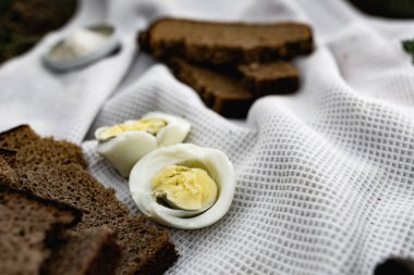 Bir dilim siyah ekmek ve yeşil çimlerin üzerinde beyaz havluyla haşlanmış tavuk yumurtası. Basit yiyeceklerle piknik yapmak. Tahta bir kutuda bitkilerle birlikte tuz ve çiçeklerin yanında..