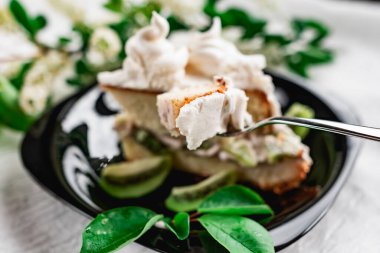 Parlak siyah bir tabakta taze kivi dilimli kremalı bir dilim pasta. Pasta, mis kokulu kiraz çiçekleriyle süslenmiş.