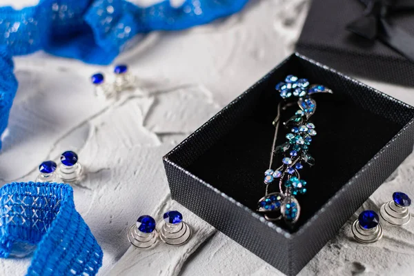 Beautiful brooch with blue and aquamarine stones and rhinestones of different sizes, metal base pins in a gift box with a black bow, around the ribbon with silver threads and springs.