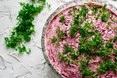 Kürk mantonun altında şişirilmiş salata ringası olan büyük kristal bir cam kase, haşlanmış pancar ve mayonez ile dolu bir Rus yemeği, üstünde yeşil su teresi yaprakları. Beyaz desenli taş zemin