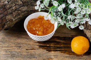 Kayısı ve şeftali reçeli tatlı olarak da portakal reçeli. Bütün bir meyvenin yanında, kayısılar şerbetle marine edilir. Eski ahşap arka plan ve kabuklu beyaz çiçekler