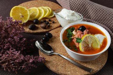 Soup Solyanka, ekşi krema, limon ve taze otlarla servis edilen çeşitli et ve domates ezmelerinin karışımı bir et çorbası. Masada siyah zeytin ve iştahınız için bir tutam taze çiçek.