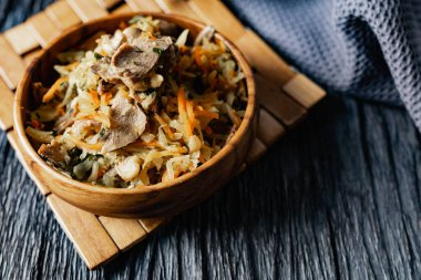 İstiridye mantarlı lahana, havuç ve soğanlı domuz dili. Tahta bir standın üzerinde, bir çatalın, bir dal çimenin ve bir peçetenin yanında, ahşap bir tabakta sıcak bir tabak. Rahatlamalı siyah arkaplan