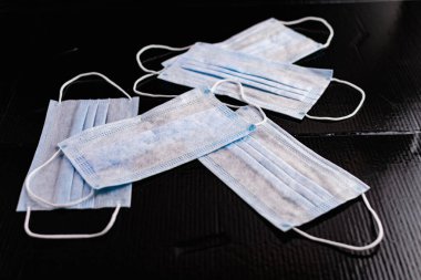 Enfeksiyon ve virüslere karşı korunmak için tek kullanımlık tıbbi maskeler. Siyah arka planda, kulaklar için elastik bantlı beyaz ve mavi katmanlar.