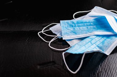 Enfeksiyon ve virüslere karşı korunmak için tek kullanımlık tıbbi maskeler. Siyah arka planda, kulaklar için elastik bantlı beyaz ve mavi katmanlar.