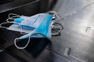 Enfeksiyon ve virüslere karşı korunmak için tek kullanımlık tıbbi maskeler. Siyah arka planda, kulaklar için elastik bantlı beyaz ve mavi katmanlar.