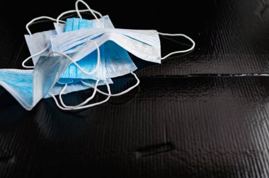 Enfeksiyon ve virüslere karşı korunmak için tek kullanımlık tıbbi maskeler. Siyah arka planda, kulaklar için elastik bantlı beyaz ve mavi katmanlar.
