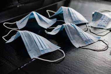 Enfeksiyon ve virüslere karşı korunmak için tek kullanımlık tıbbi maskeler. Siyah arka planda, kulaklar için elastik bantlı beyaz ve mavi katmanlar.
