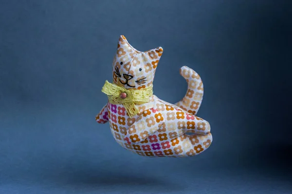 Flying reddish-brown cat. A handmade toy with a bow around his neck. From a cloth with a pattern, soft. Kind, pleasant, smiling cat.
