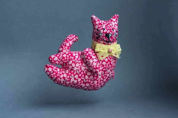 Flying red cat. A handmade toy with a bow around his neck. From a cloth with a pattern, soft. Kind, pleasant, smiling cat.