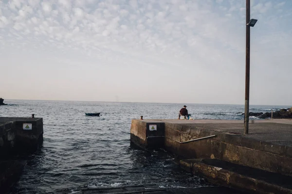 One man sitting on concrete pier and fishing