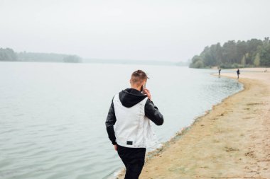 Kumsalda, dikiz yürürken Smartphone ile konuşan şık genç adam