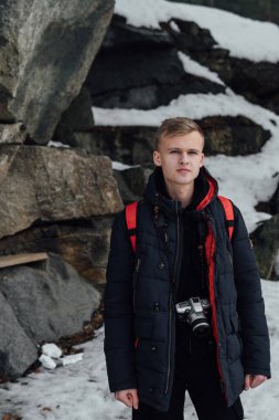 Karla kaplı cliff tarafından poz ve kameraya bakarak boynunda asılı kamera ile genç adam
