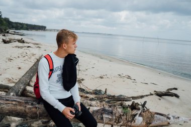 Genç backpacker elinde kamerayla woods Nehri sahilinde üzerinde dinlenme