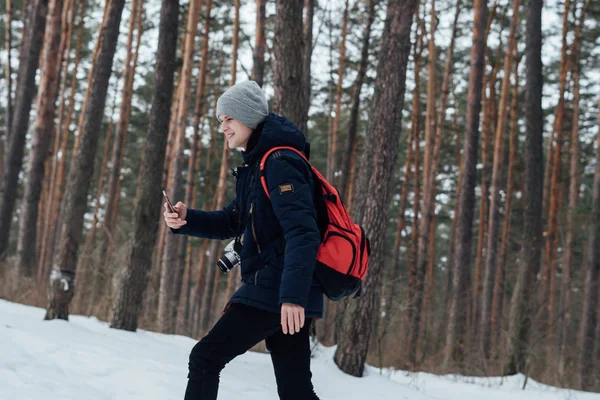 Neşeli backpacker smartphone vasıl kış woods ile yürüme yan görünüm 