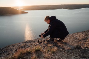 Çömelme ve güneşli Nehri sahilinde bitkilerin çekimi genç fotoğrafçı yan görünüm