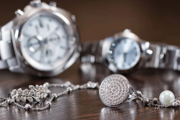 Zilveren Ringen en ketting liggen op achtergrond chrome horloges — Stockfoto