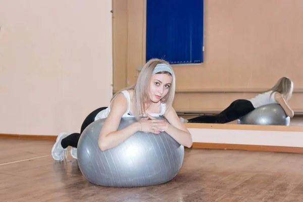 Chica joven agraciada hace ejercicios de fitness en una pelota de ejercicio — Foto de Stock