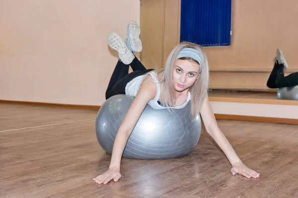 Chica joven agraciada hace ejercicios de fitness en una pelota de ejercicio — Foto de Stock