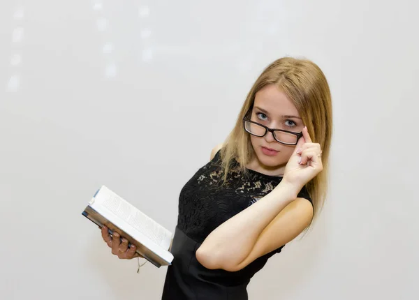 Νεαρή γυναίκα στο μαύρο φόρεμα με γυαλιά, διαβάζοντας ένα βιβλίο — Φωτογραφία Αρχείου