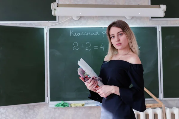 Молода чарівна блондинка вчителька стоїть в класі зі стеком о — стокове фото