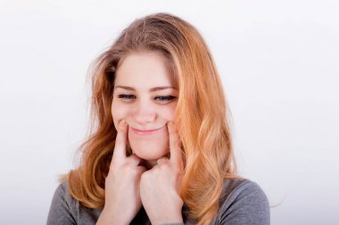 beautiful young woman forcing a smile, holding her fingers near  clipart
