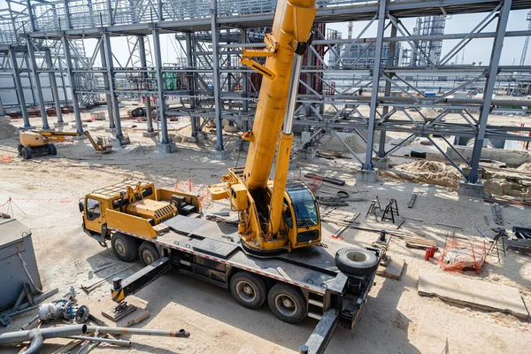 A large yellow car crane stands on the construction site of an oil refinery
