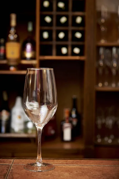 A glass on the bar in the background of a bar with bottles of alcohol