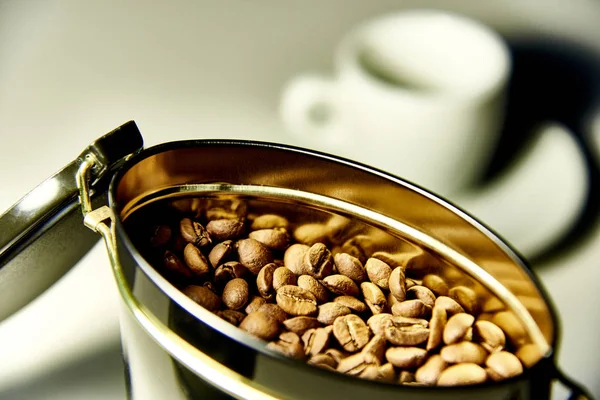 An open can with coffee beans on the background of a cup and a saucer