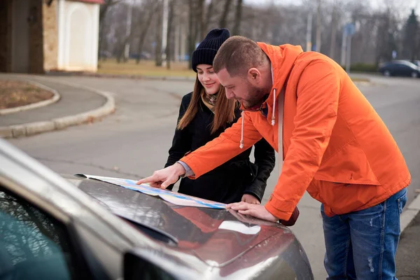 Young people with a map near a car on the road.