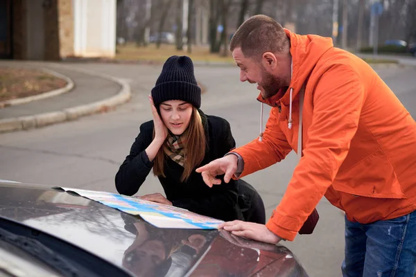 Young people argue near a car with a map on the road.