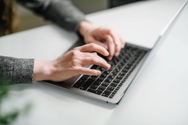 Eller üstünde belgili tanımlık laptop klavye metin yazarak genç bir kadın. Gri elbise. Evde office el klavye üzerinde çalışan kadın kapatın. Beyaz masa, sığ derinlik-in tarla. 