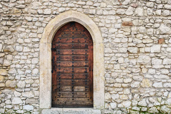 Stone fortress castle wall of a medieval castle, an old wooden closed arcade door with iron rivets.