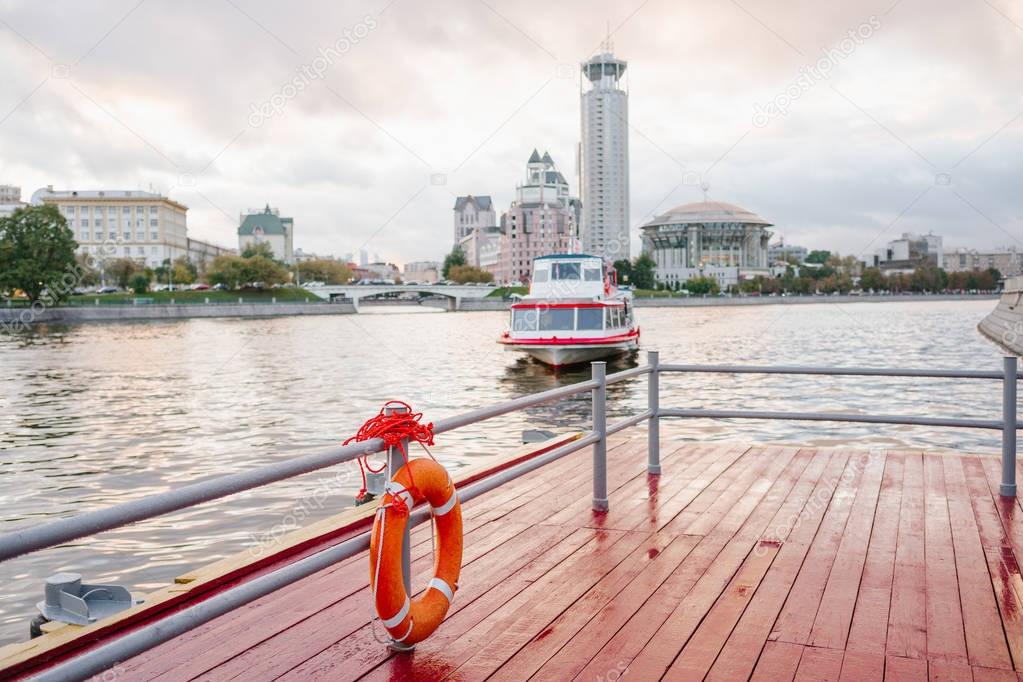 Orange lifebuoy on the river dock. Safety on the water. The river cruise ship and the Moscow International Performing Arts Center on the background. 