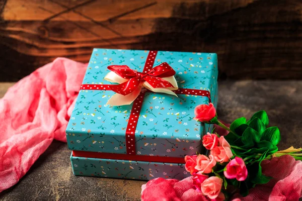 Blue gift box with flowers and red ribbon with rose flowers on b